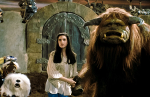 SF – Celebrate 40 Years of Labyrinth | Aug 22nd A young woman stands next to a large horned creature and two fantasy animals in front of a stone door in a fantasy setting.